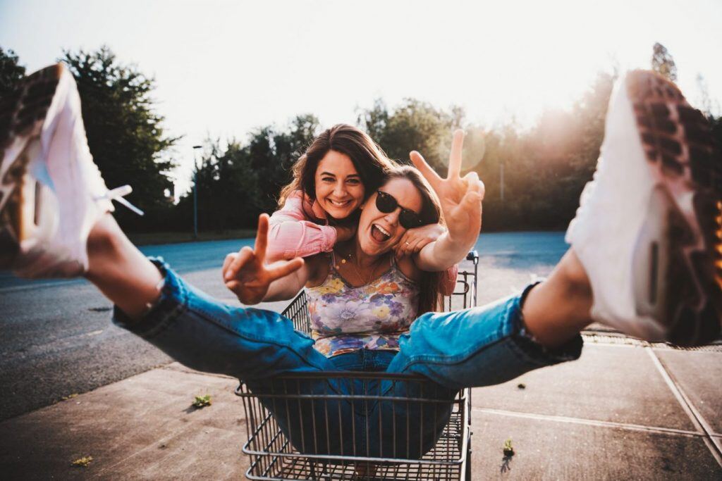 friends smiling while sitting in a shopping cart