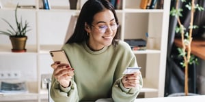 person-in-sweater-looking-at-credit-card-and-phone-happily