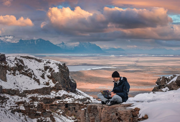 winter-hiker-on-laptop-on-top-of-mountain