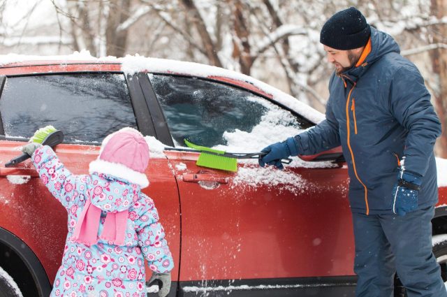 family wiping the snow off their new car